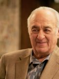 Улыбающийся Хеш Рабкин в светло-коричневом пиджаке и узорчатой рубашке.
